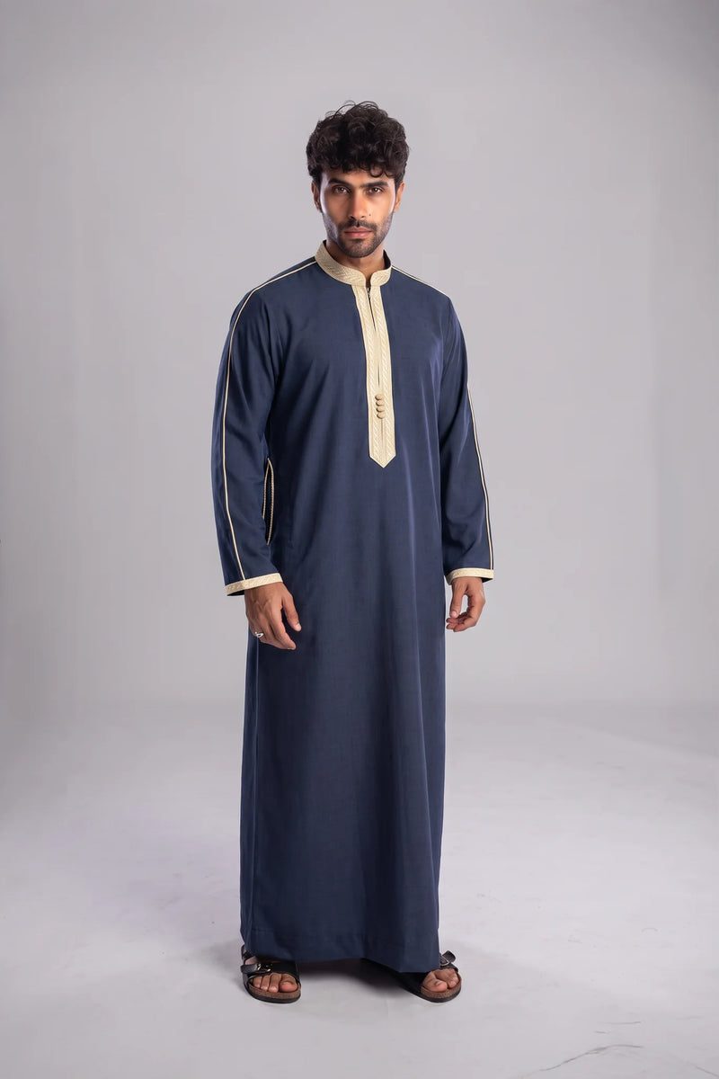 A man modeling a long-sleeved navy blue traditional robe with beige trim and a beige zipper placket, standing against a neutral gray studio background.